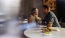 a man and woman sitting at a table with food and drinks